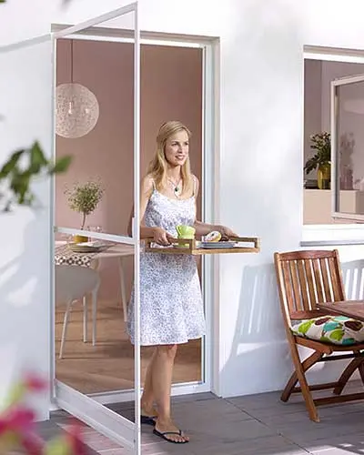 Insektenschutz – Frau geht mit Tablett durch Tür mit Insektenschutz